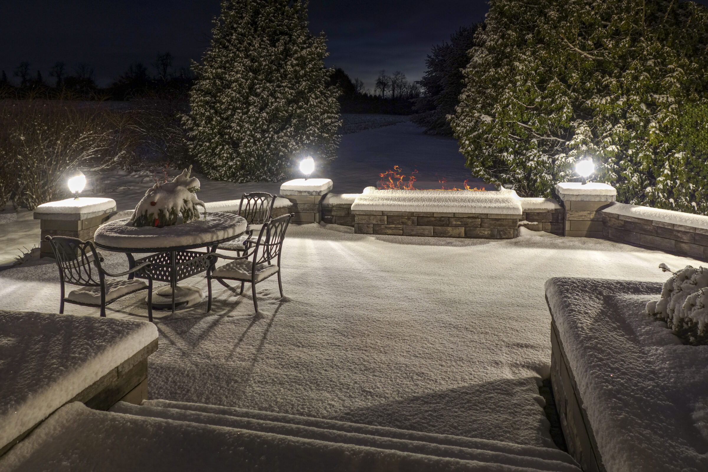 Snow-covered patio with chairs and table at night