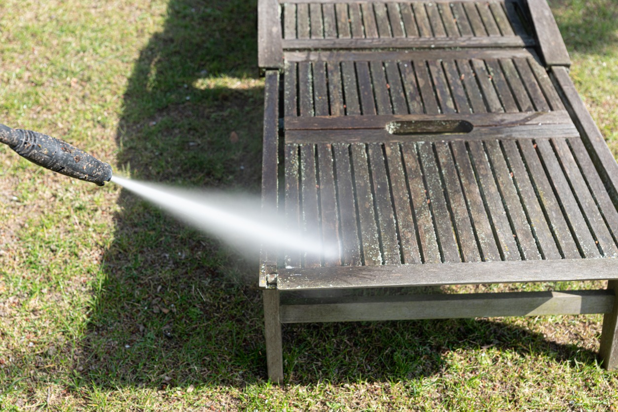 Pressure washing wooden patio table on grass.