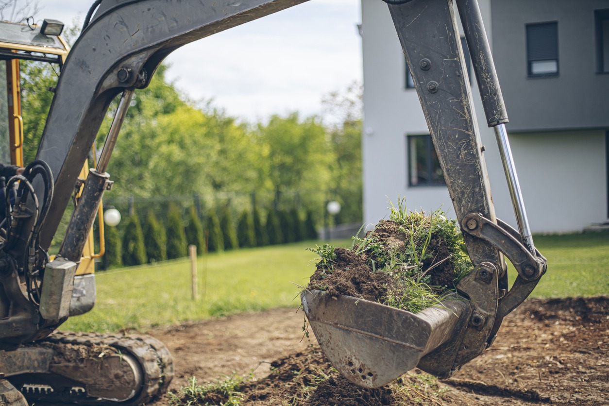 Excavator digging soil near house construction site.