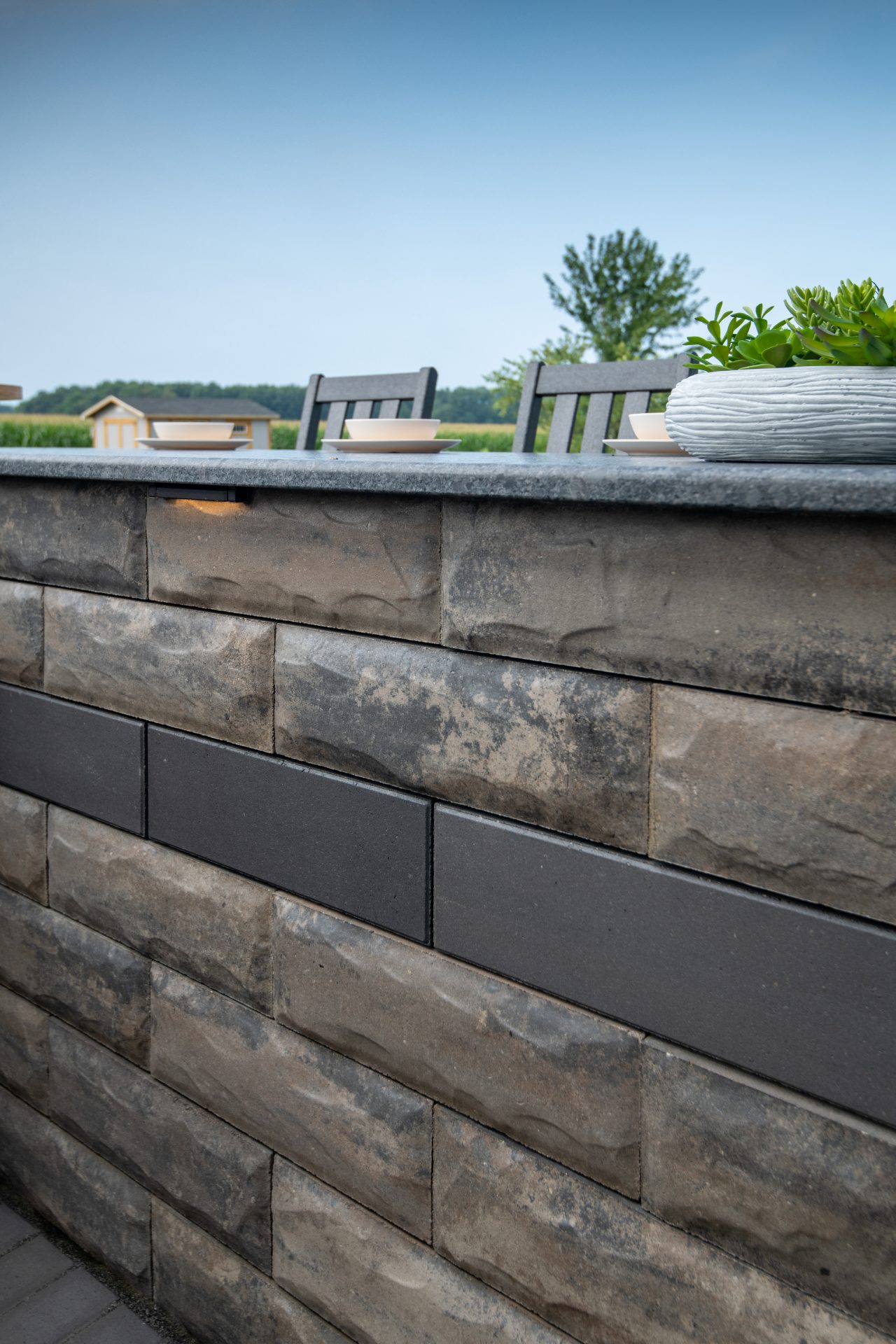 Outdoor stone wall with chairs and plants.